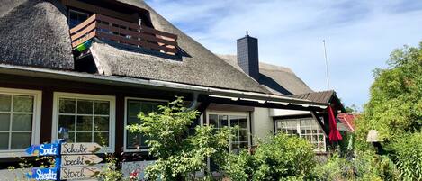 A traditional house with a thatched roof, a wooden balcony, and a stone wall.