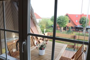 Une vue à travers une fenêtre donnant sur une terrasse en bois, avec une plante en pot et une décoration en forme de bicyclette.
