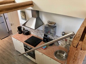 A compact kitchen with a built-in stove, a coffee maker, and a hanging basket.