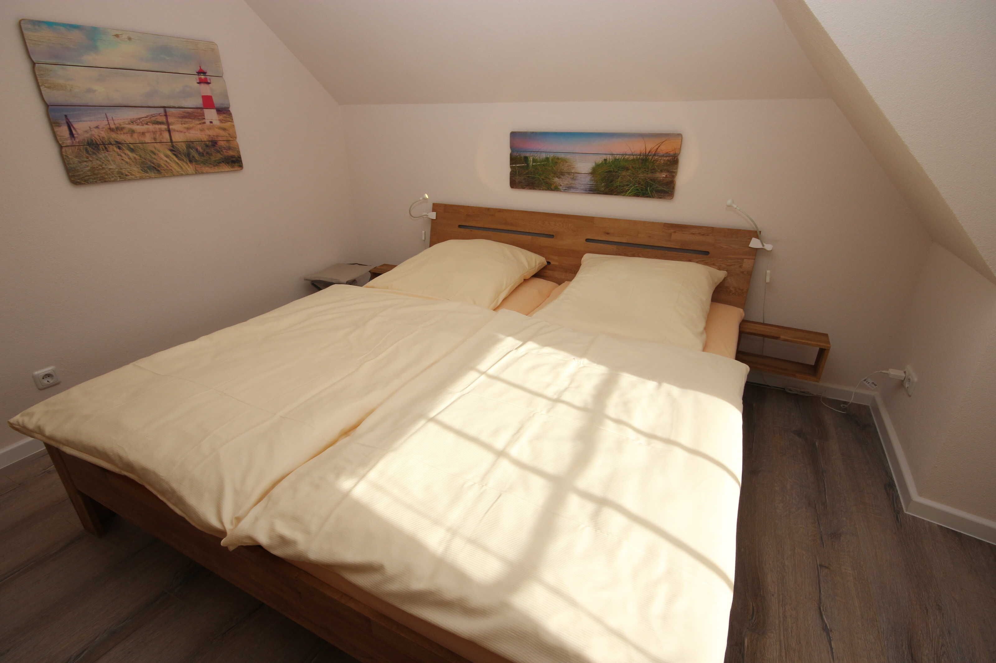 A bedroom with a wooden bed, two bedside tables, a nightstand, a painting of a landscape, and a sloped ceiling.