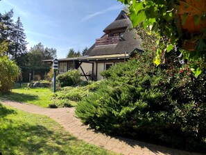 Une maison au toit de chaume, entourée d’une végétation luxuriante et bordée d’un chemin pavé.