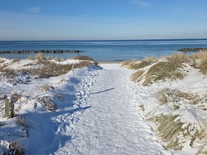 A snow-covered path leading to a body of water with a clear sky.