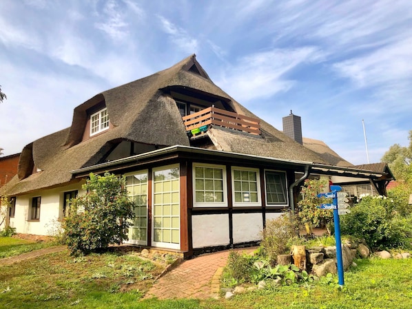 A traditional house with a thatched roof, a wooden balcony, and a garden with a pathway.