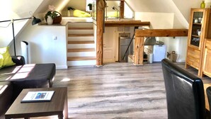Un dormitorio en el ático con cama alta, escritorio, silla, kitchenette pequeña y escalera.