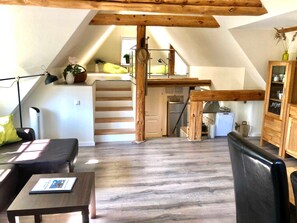 Une chambre aménagée dans les combles, avec un lit en mezzanine, un bureau, une chaise, un petit coin cuisine et un escalier.