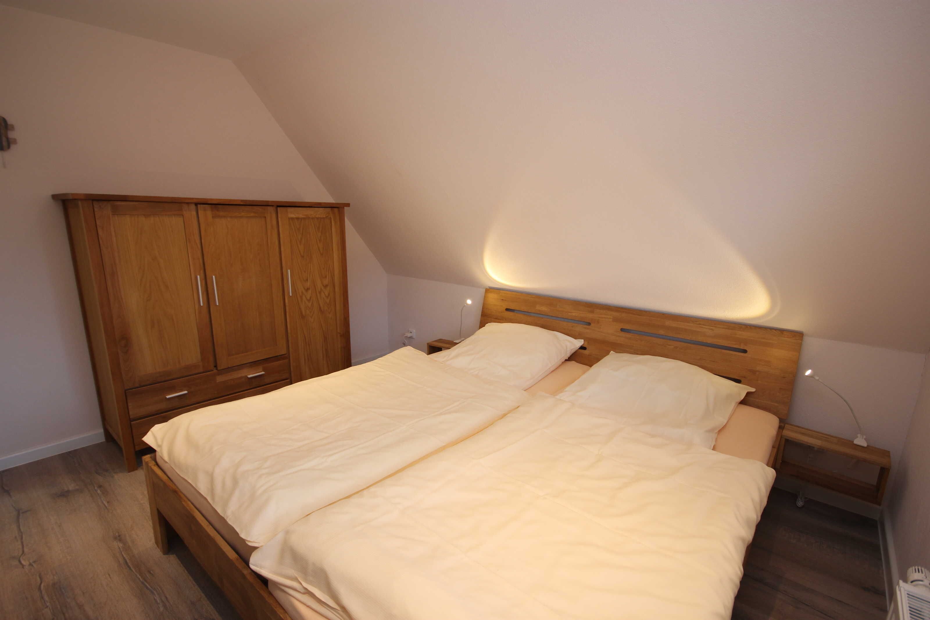Ein Schlafzimmer mit einem hölzernen Bett, einem Nachttisch, einem Kleiderschrank und einer schrägen Decke.