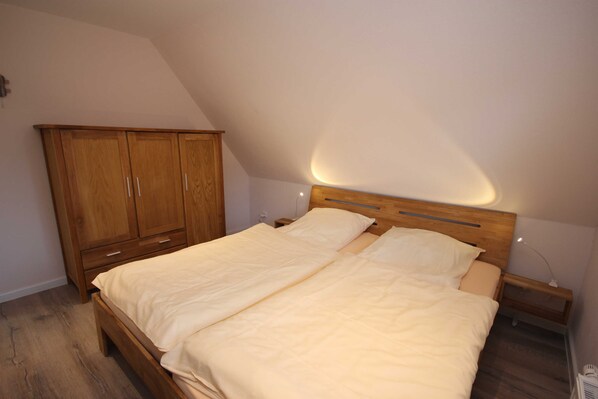 Un dormitorio con cama de madera, mesita de noche, armario y techo inclinado.