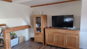 Un mueble de madera con un televisor, un aparador de vidrio con tazas y un taburete de madera.
