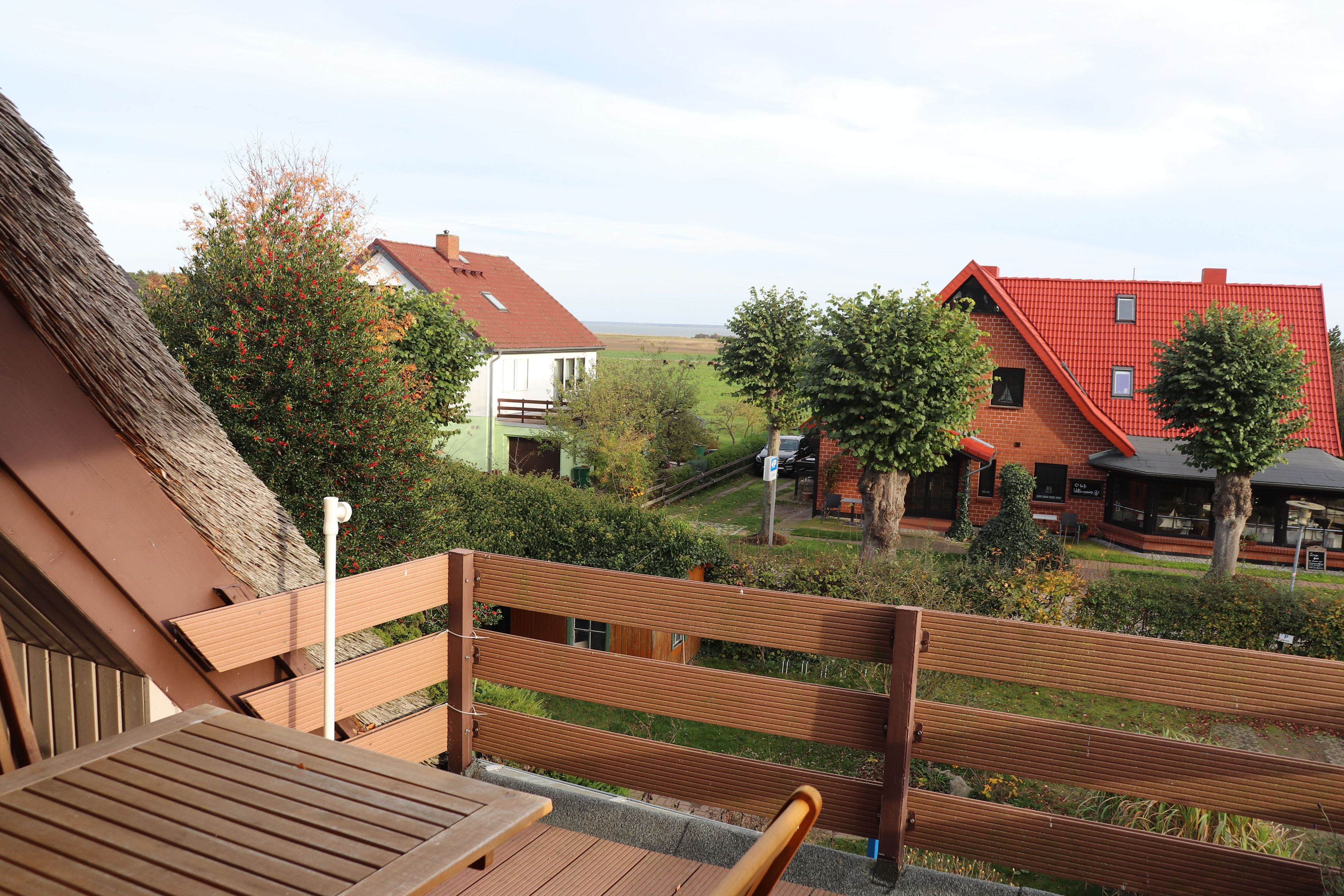 A wooden deck with a bench, a table, and a view of houses and greenery.
