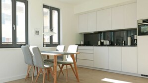A modern kitchen with white cabinets, a dining table with chairs, and a window providing natural light.
