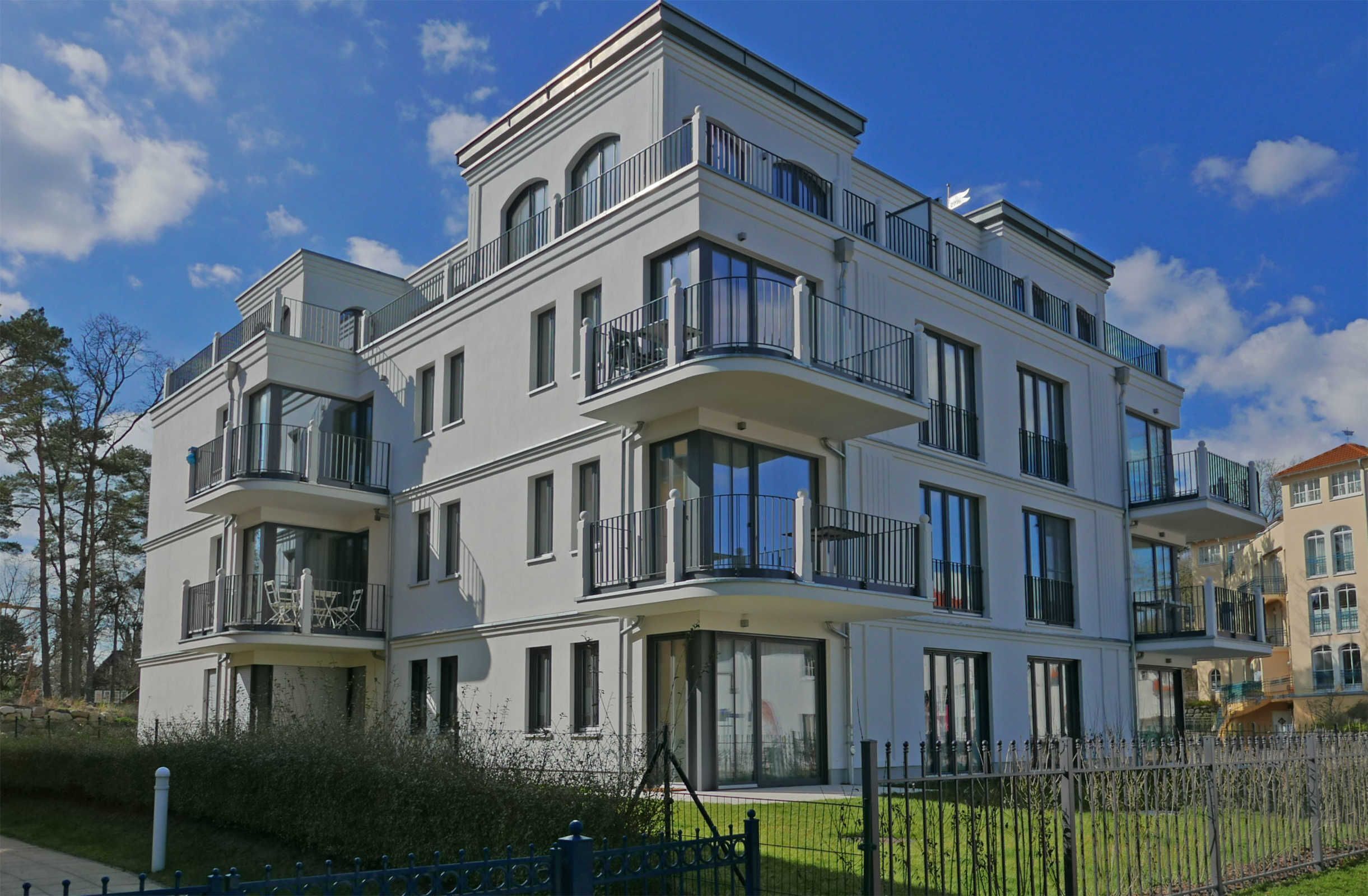 Un edificio residencial de varios pisos con balcones, ventanas amplias y un césped bien cuidado.
