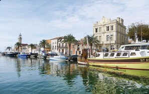 A marina with boats docked, a prominent building with classical architecture, and a lighthouse in the background.