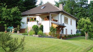 A two-story house with a sloped roof, a front porch, and a small balcony with potted plants.