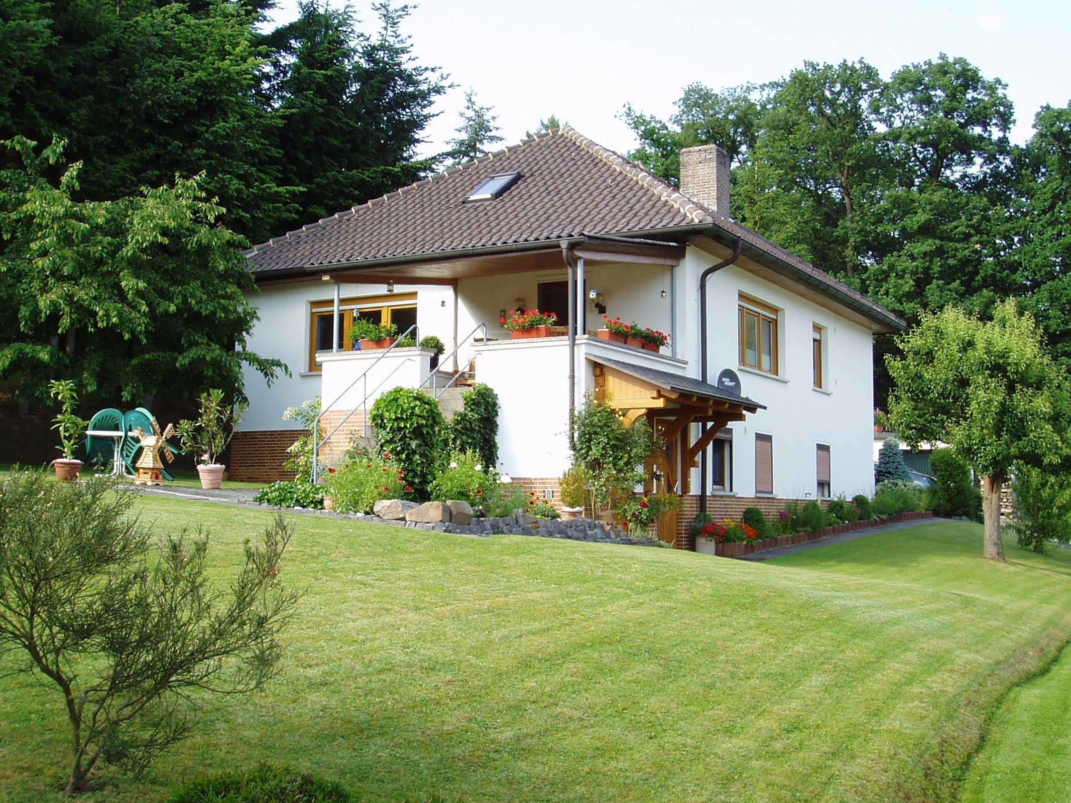 A two-story house with a sloped roof, a front porch, and a small balcony with potted plants.