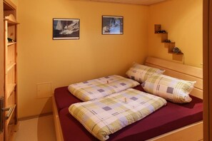 A room with a bed, two framed pictures on the wall, a wooden shelf with a clock, and a door with a handle. - Apartment In Marmot - Apartment in marmot (Edertal)