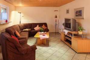A cozy living room with a brown sofa, a wooden coffee table, a TV, and a small plant. - Apartment In Marmot - Apartment in marmot (Edertal)