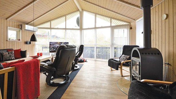 A cozy living room with a high ceiling, wooden walls, and large windows. There are two comfortable chairs, a sofa, and a television.