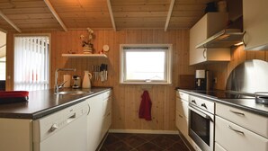 A compact kitchen with wooden walls, a window, and basic amenities like a sink, stove, and coffee maker.