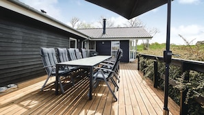 A covered outdoor deck with a dining table and chairs, a small building with a tiled roof, and a wooden railing.