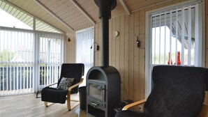 A cozy room with a wood-burning stove, two black chairs, and a glass table.