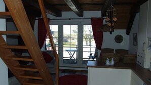 A cozy kitchen with a wooden staircase, a dining area with outdoor seating, and a large window with curtains.