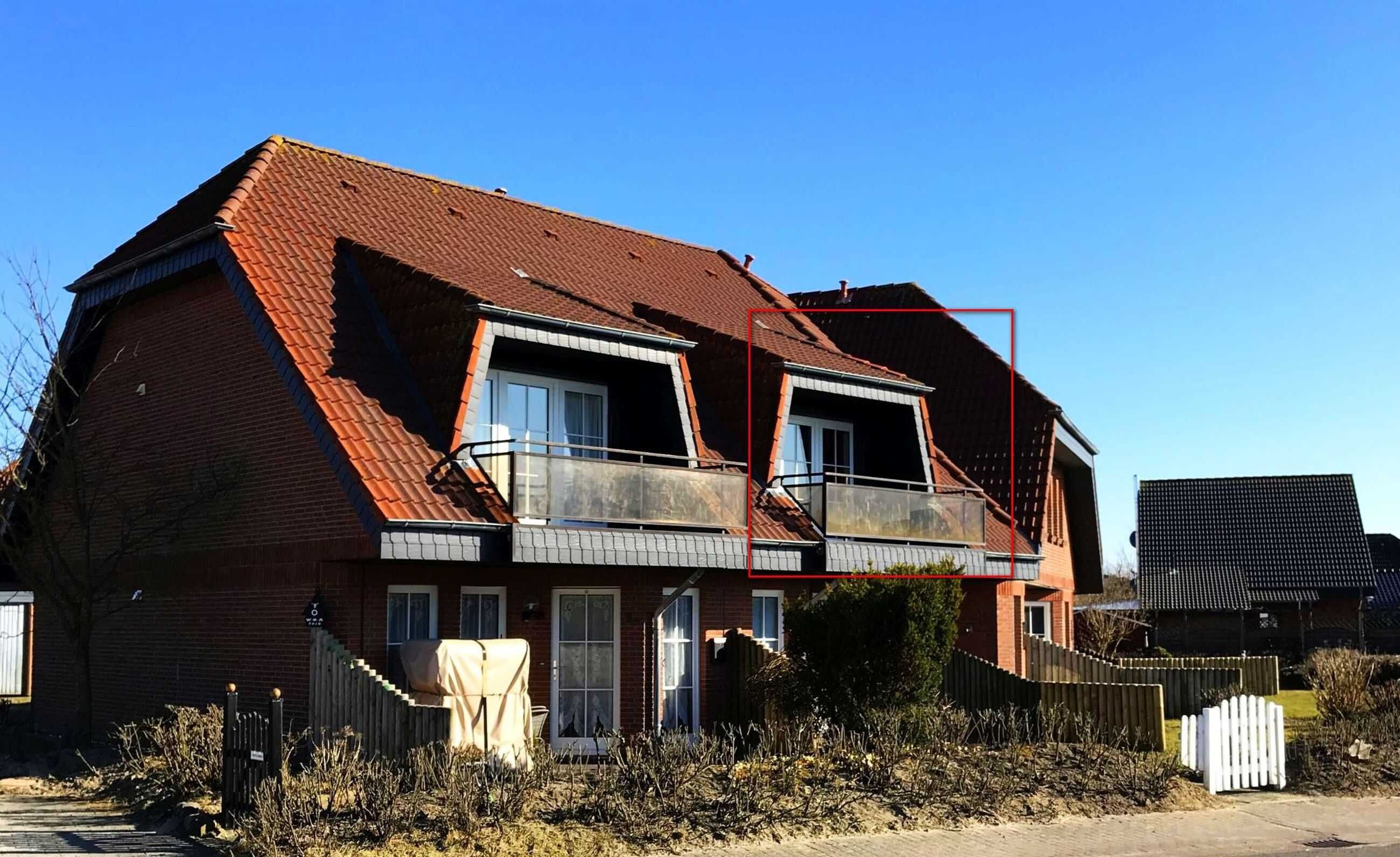A two-story house with a red-tiled roof, a balcony on the second floor, and a fenced yard.