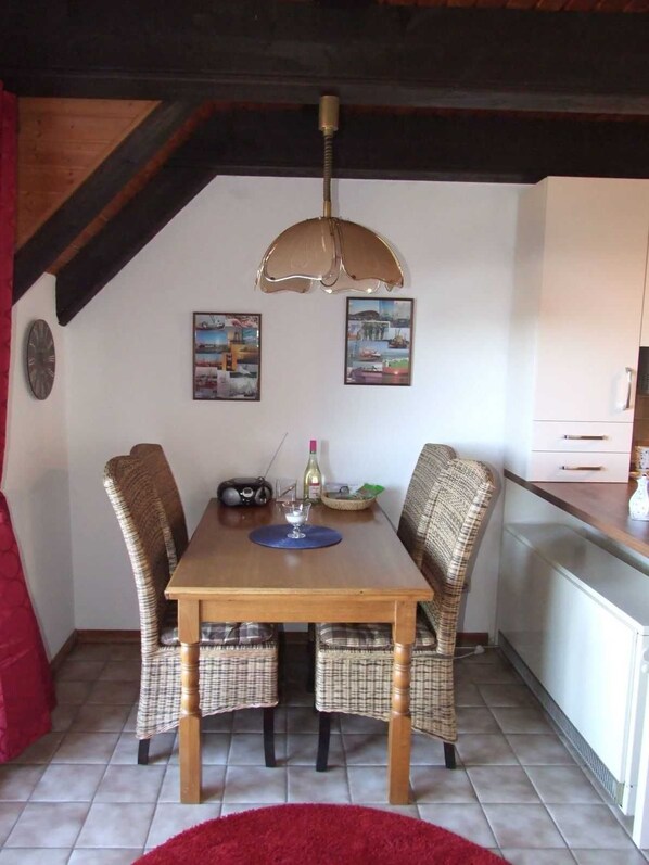 A dining area with a wooden table, wicker chairs, a red rug, and two framed pictures on the wall.