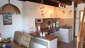 A compact kitchen with white cabinets, a microwave, a coffee maker, and a sink. There is a dining area with a table and chairs.