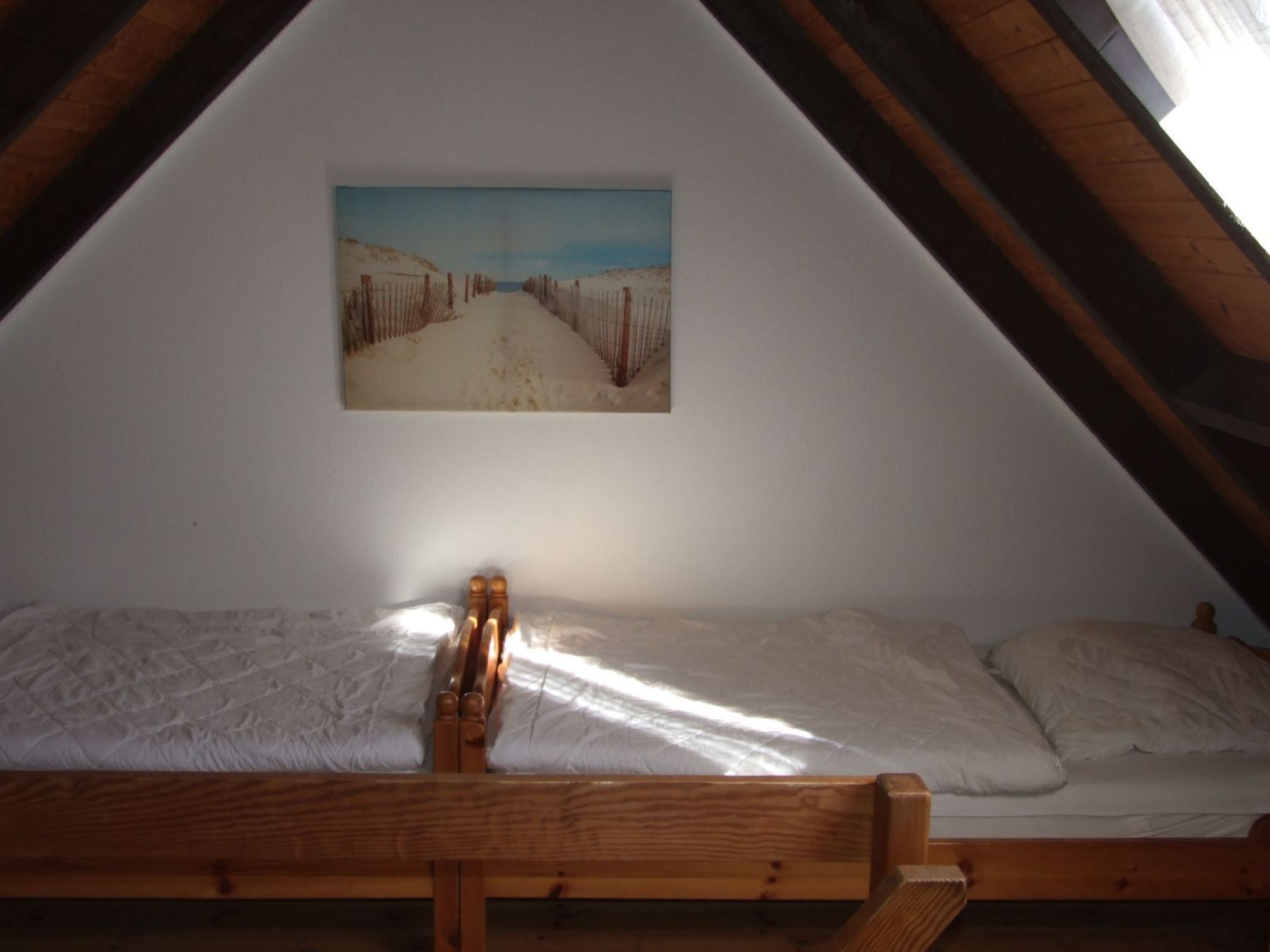 A bedroom with a wooden bed, white bedding, and a painting of a snowy landscape on the wall.
