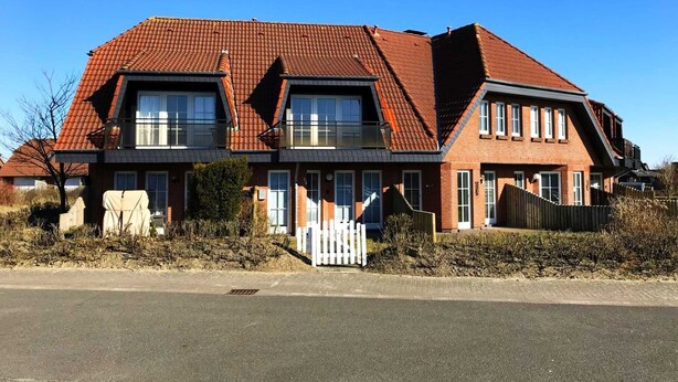 A two-story house with a red-tiled roof, large windows, and a white picket fence.