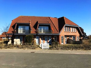 A two-story house with a red-tiled roof, large windows, and a white picket fence.
