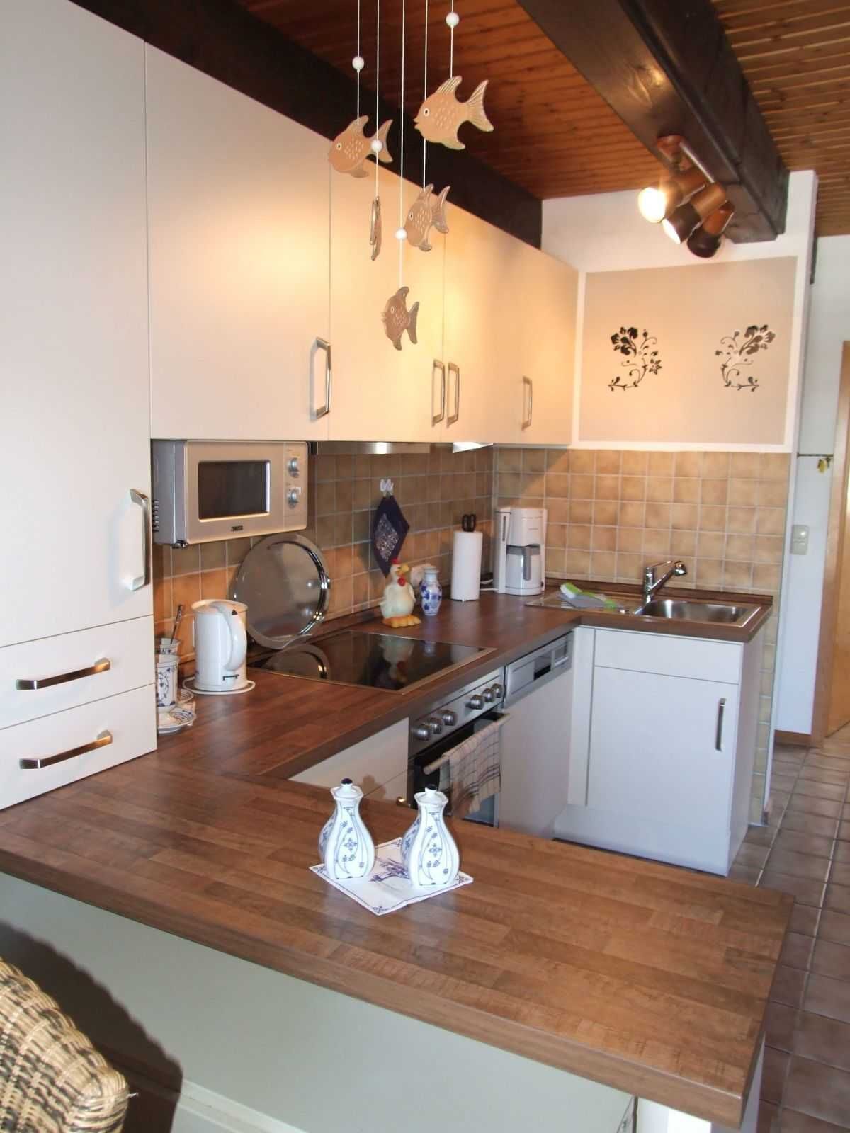 A modern kitchen with white cabinets, a wooden countertop, a built-in oven, and a coffee machine.