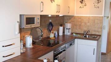A modern kitchen with white cabinets, a wooden countertop, a built-in oven, and a coffee machine.