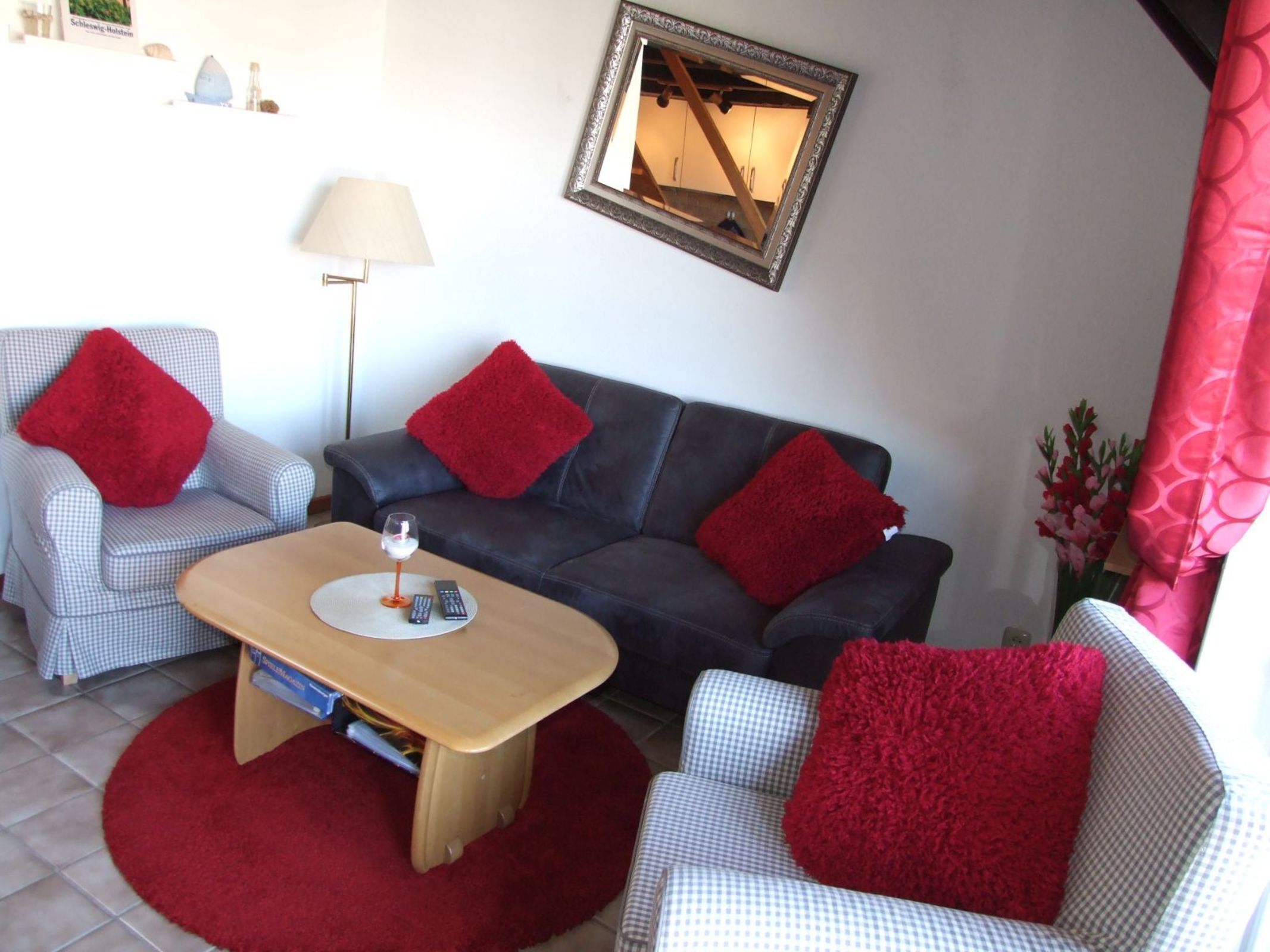 Un salon avec un canapé à carreaux, un canapé foncé et une table basse en bois. On trouve des coussins rouges sur les canapés et une lampe sur le sol.