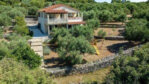 Une maison en pierre dotée d’un balcon, entourée d’oliviers et d’un mur de pierres.