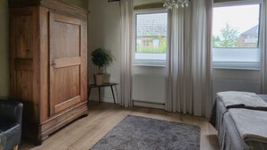 Een kamer met een houten garderobe, een kamerplant, een radiator, een raam met gordijnen en een bed met een deken.