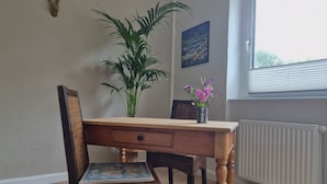 Een eethoek met een houten tafel, twee stoelen, een potplant en een raam met zonwering.