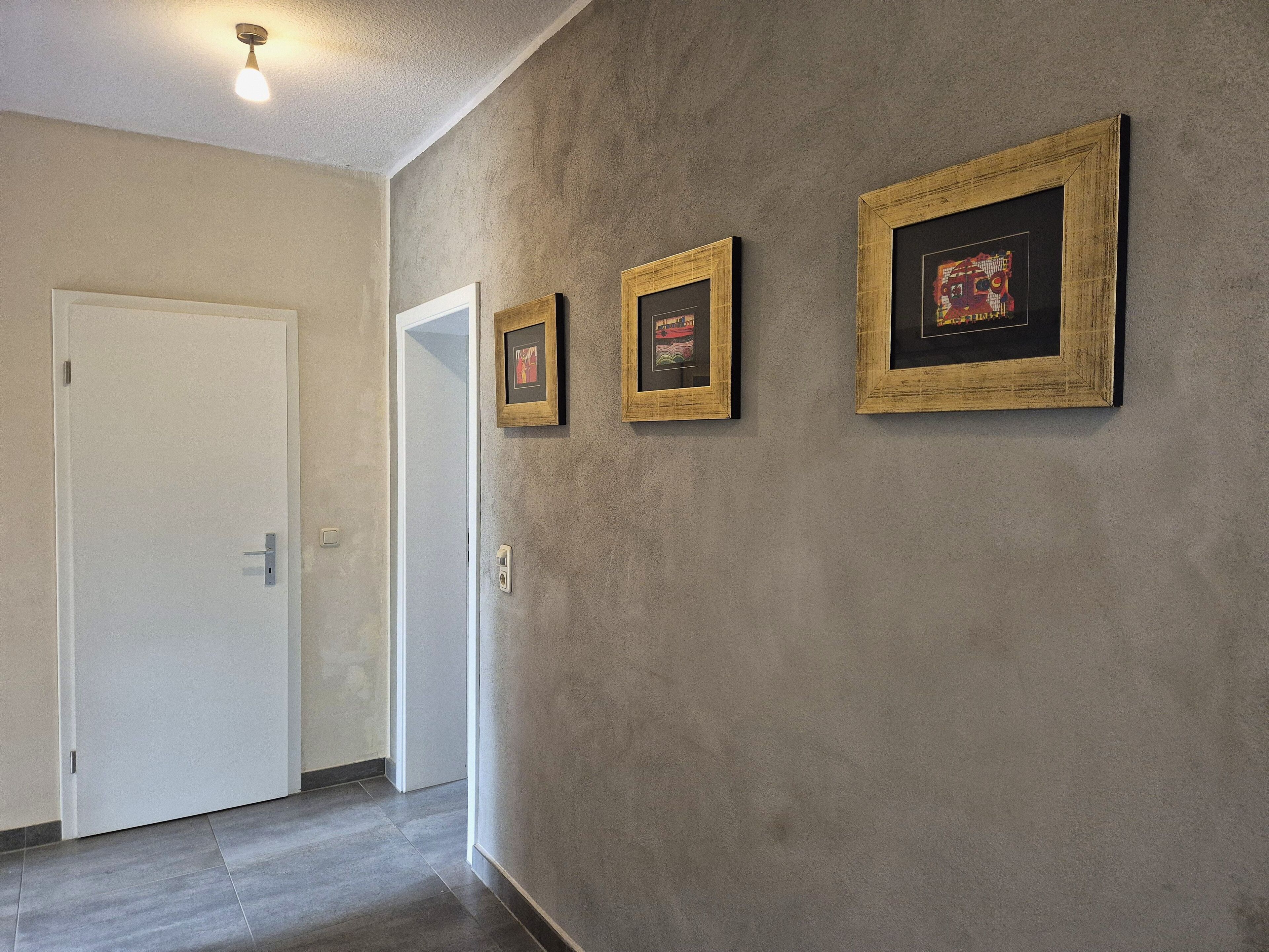 Un pasillo con una puerta blanca, una lámpara y tres cuadros en la pared.