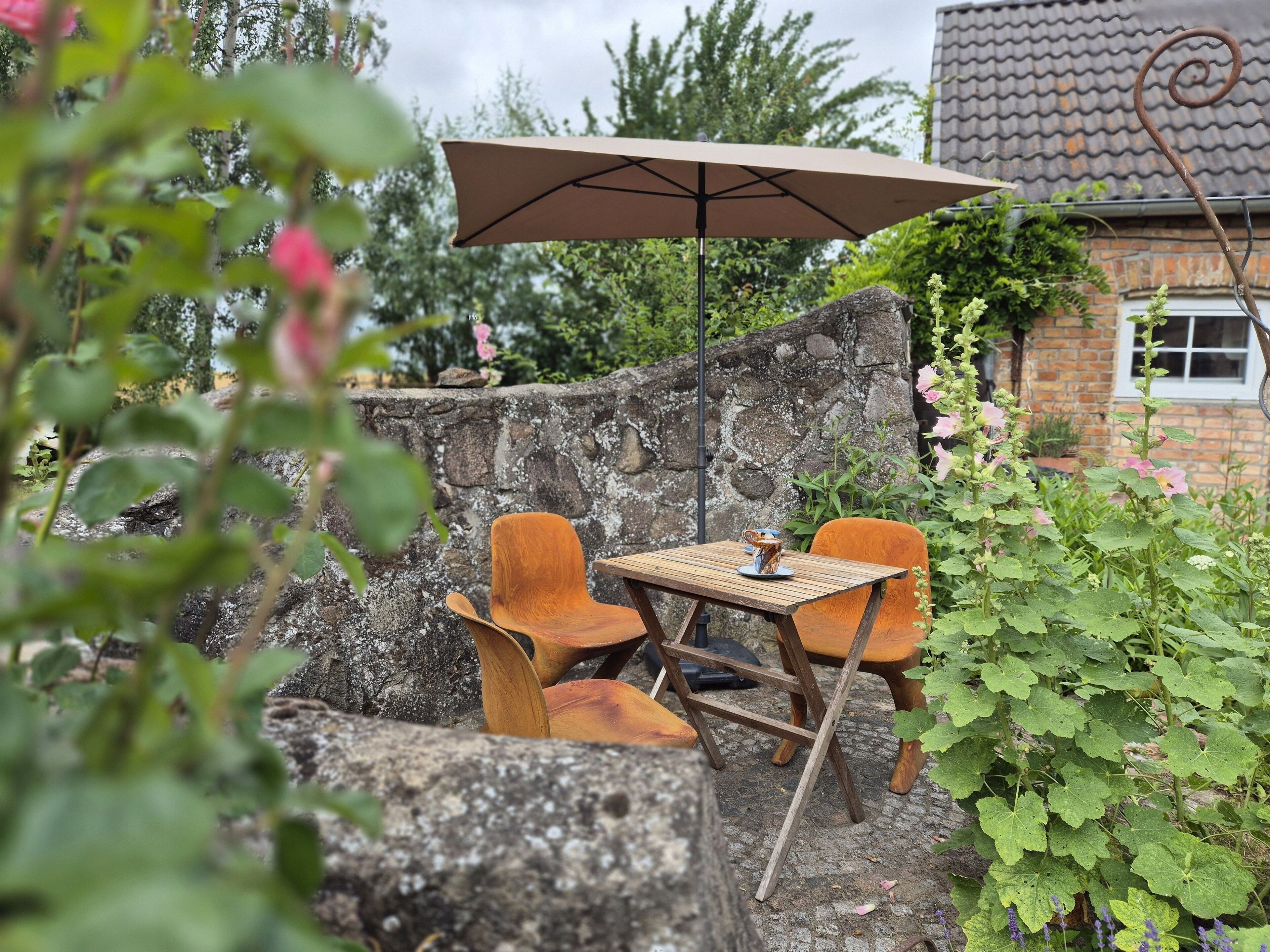 Un espacio de estar al aire libre rústico con una mesa y dos sillas, un muro de piedra y una casa en el fondo.