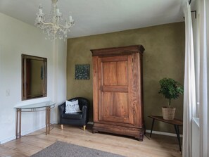 Ein Zimmer mit einem Holzschrank, einem schwarzen Ledersessel, einem Glastisch, einer Kristallleuchter und einer Kübelpflanze.