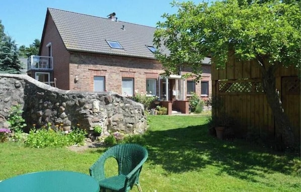 A brick house with a stone wall, a wooden fence, and a green chair in the yard. - Vacation apartment 1 - Green idyll (Borrentin)