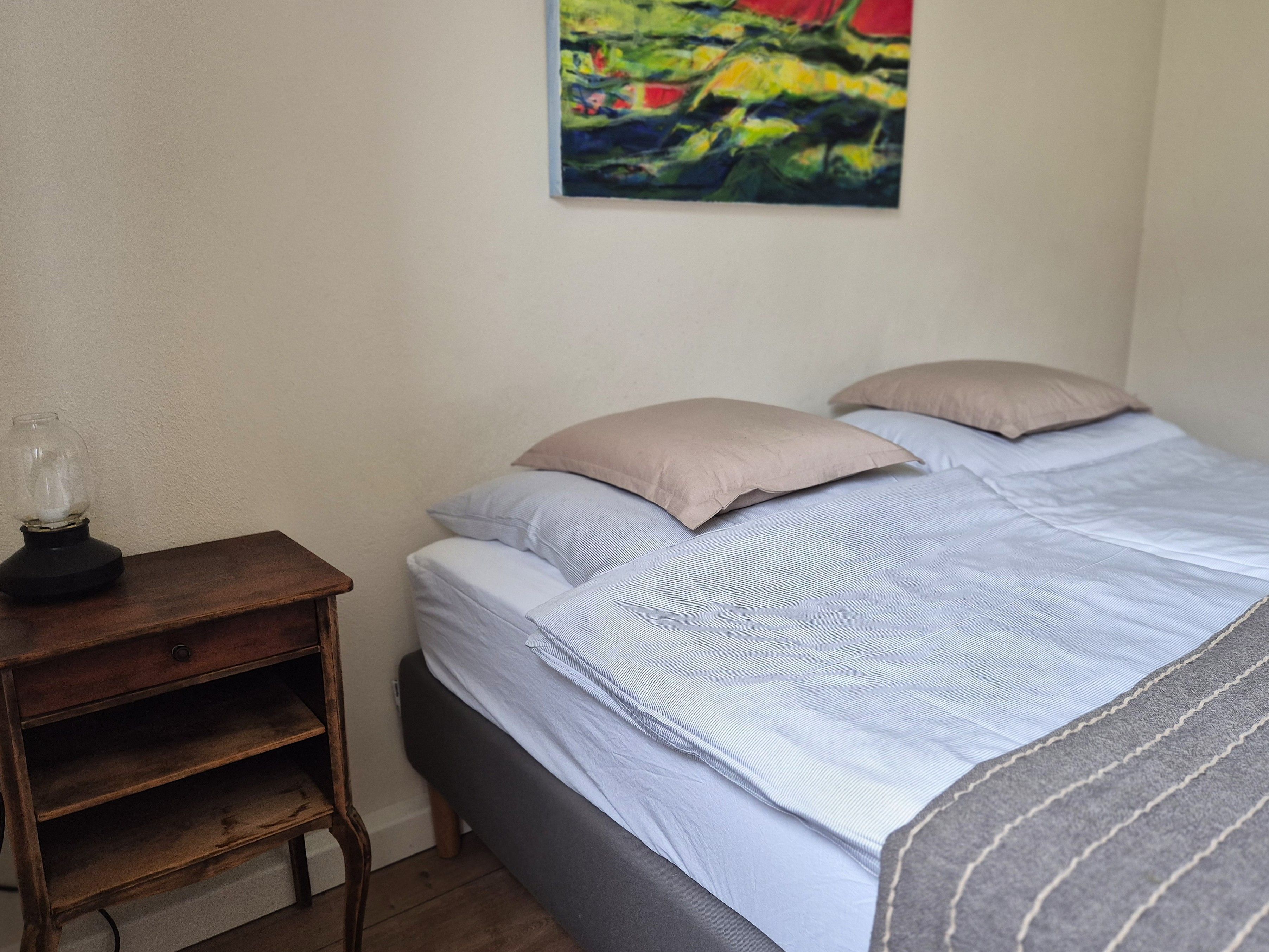 A bedroom with a bed, pillows, a nightstand, and a wall-mounted painting.