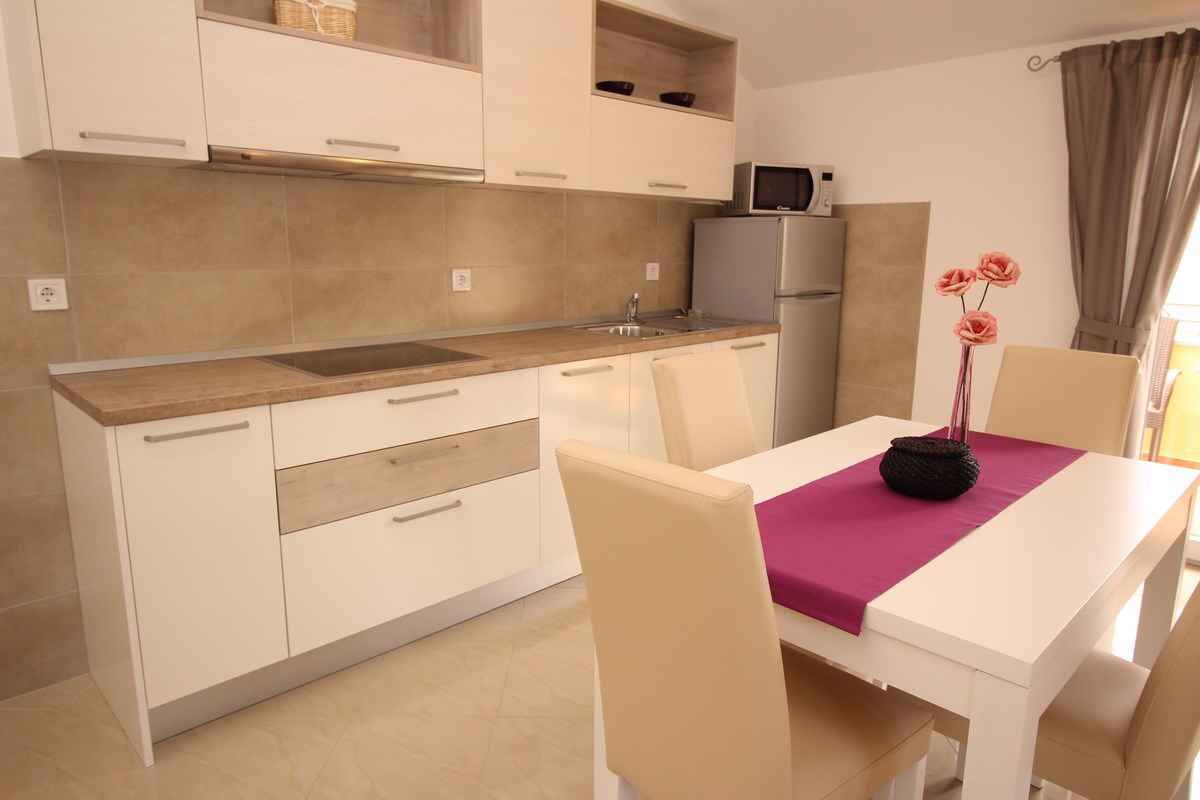 A modern kitchen with white cabinets, a microwave, and a sink. There is a dining table with chairs and a vase with flowers.