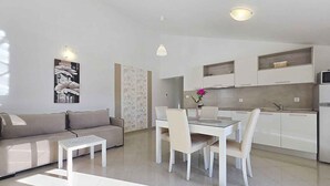 Una sala de estar moderna con sofá, mesa de centro, mesa de comedor, sillas y una zona de cocina con armarios y refrigerador.