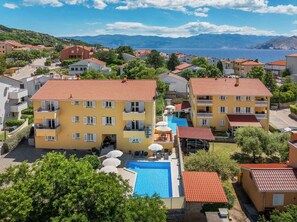 A residential area with a large building featuring a swimming pool, balconies, and a view of the sea. - Holiday apartment mit Pool (Baška)
