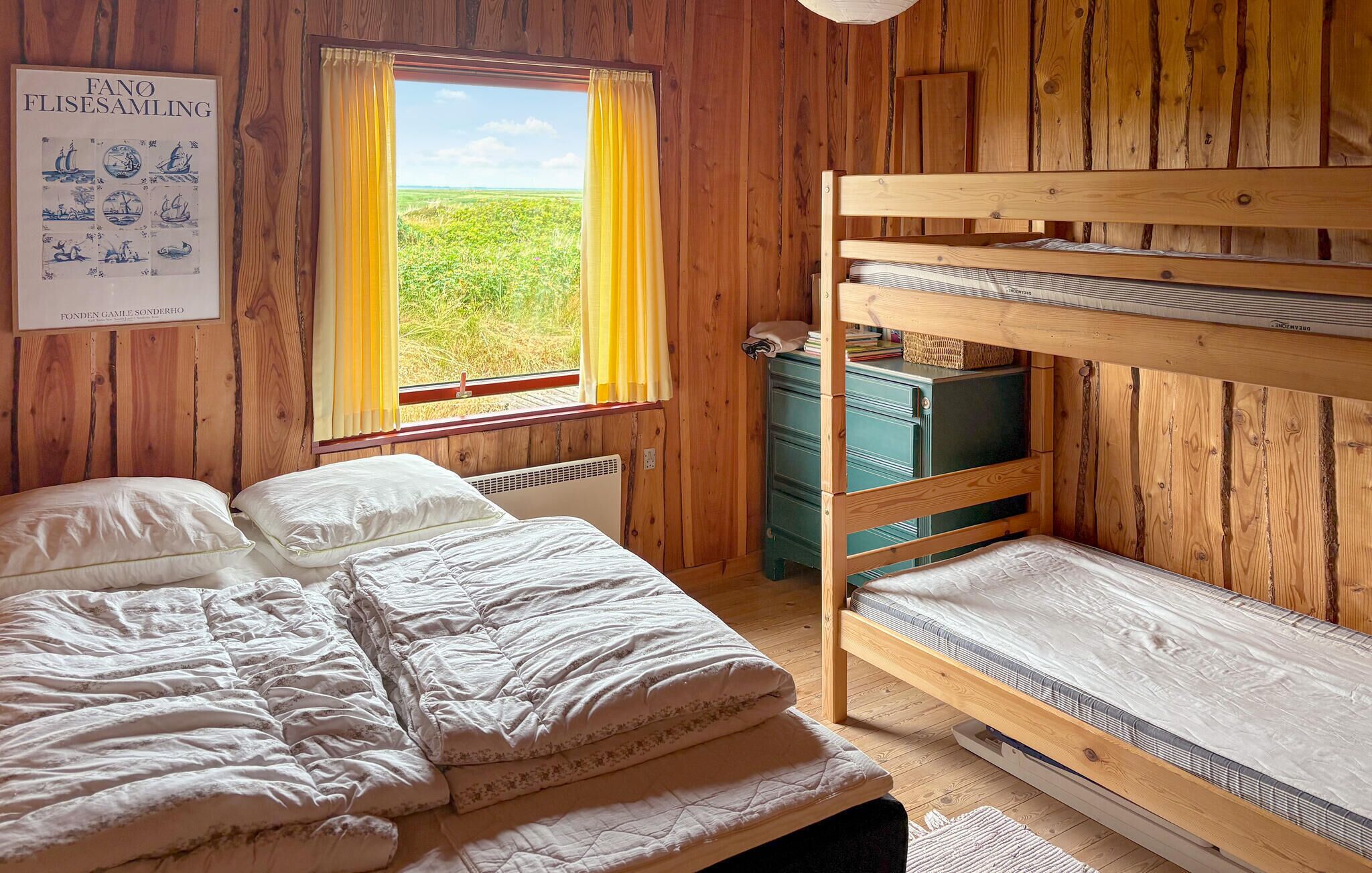 Une chambre avec des lits superposés, une fenêtre donnant sur un champ verdoyant, une affiche au mur et une commode.