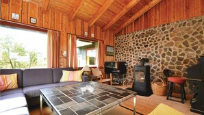 Et hyggeligt sommerhusinteriør med en stenvæg, træloft, en sofa, et fjernsyn og en pejs.