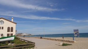 A coastal building with a green boat in front, a clear sky, and a beach with a signboard.