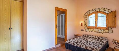 A bedroom with a bed, a wardrobe, a window with a stone frame, and a door leading to another room.