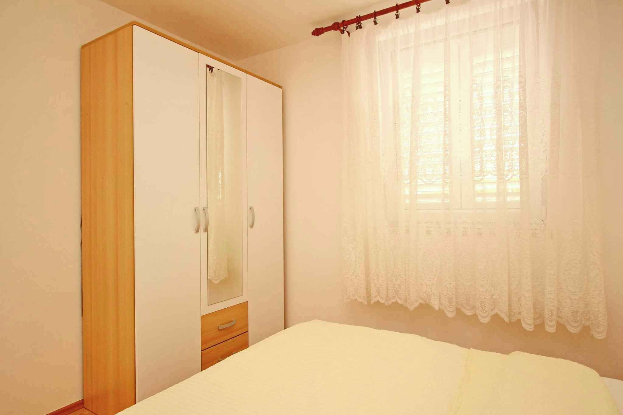Ein Schlafzimmer mit einem Holzschrank, einem Bett mit weißer Decke und einem Fenster mit Spitzenvorhängen.